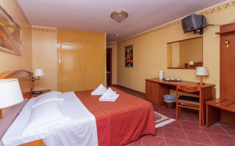 Cozy hotel room with a double bed, desk, closet, warm yellow walls, red floors, and inviting decor.