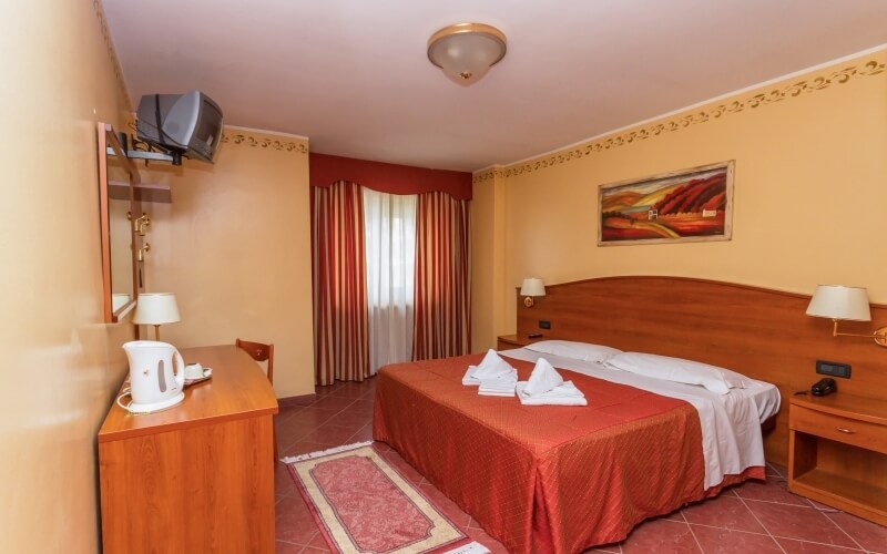 Cozy hotel room with a king-sized bed, vibrant orange and red decor, nightstands, dresser, and striped curtains.