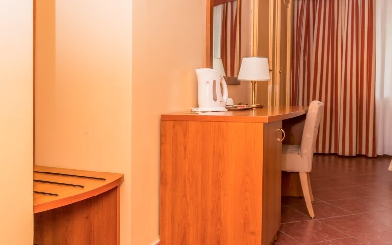 Camera d'hotel serena con scrivania in legno, lampada, tende a righe rosse e bianche, e pareti gialle accoglienti.