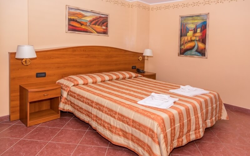 Cozy bedroom with a bed, nightstands, artwork, light peach walls, and red tile flooring, featuring a striped comforter.