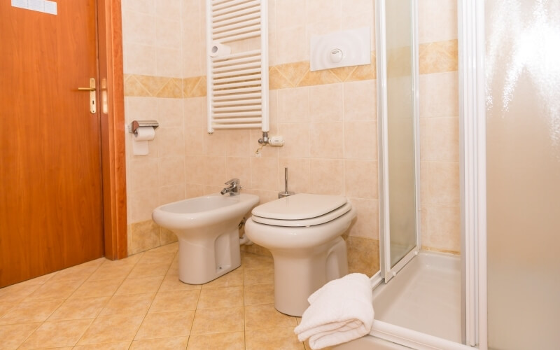 Immagine di un bagno con toilet, bidet, doccia, asciugamano piegato, radiatore e porte in legno. Piastrelle beige.