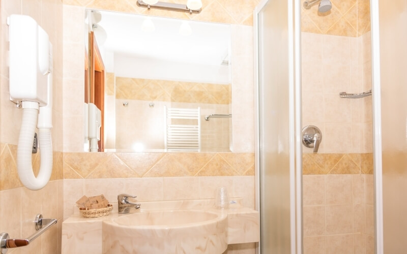 Serene beige bathroom with a large mirror, sink, shower, hair dryer, and toiletries, exuding calmness and warmth.