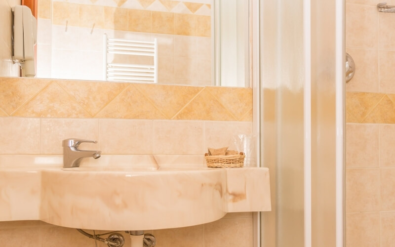 A clean bathroom with a white marble sink, silver faucet, wicker basket, and a partially open shower door, featuring yellow tiles.