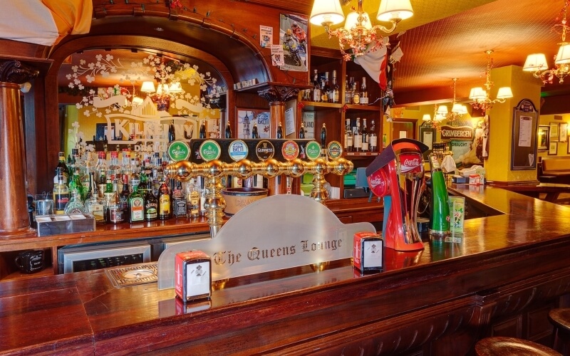 Pub tradizionale con bar in legno, sei birre, lampadari decorativi e atmosfera accogliente per socializzare.