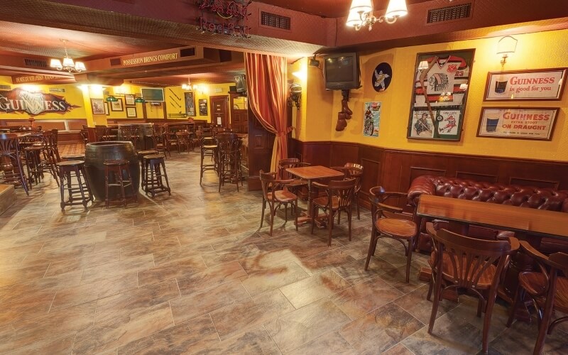 Bar spazioso e accogliente con pareti gialle, divano in pelle marrone, tavoli e decorazioni, ideale per socializzare.