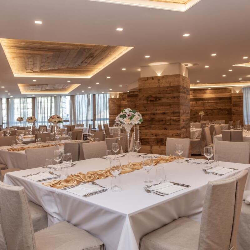 Elegant banquet room with white tablecloths, centerpieces, and warm lighting, set for dining with rustic wooden walls.