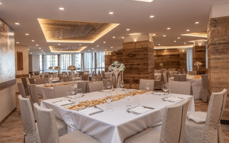Elegant dining room with white tablecloths, gold runners, and floral centerpieces, set for a formal event.