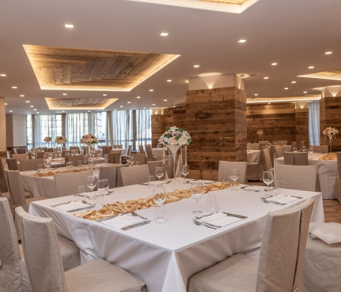 Elegant formal dining room with a long table set, beige chairs, floral centerpieces, and natural light from large windows.