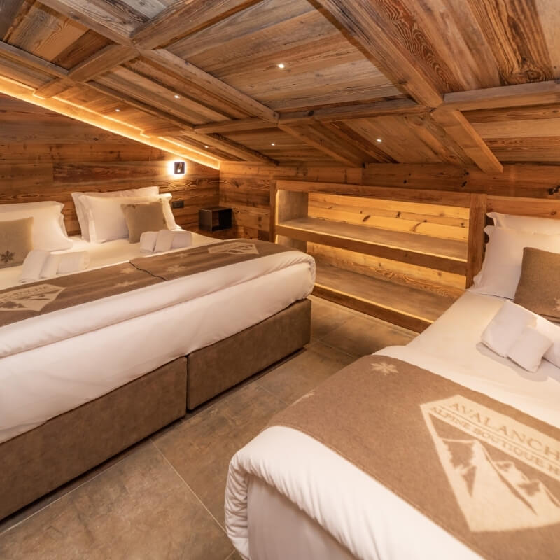 Camera d'albergo rustica con due letti, soffitto in legno, pareti in legno e illuminazione calda.