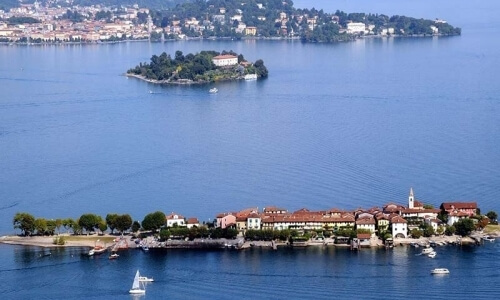 Serene island scene with lush trees, buildings, and sailboats on calm waters, set against a distant landmass.