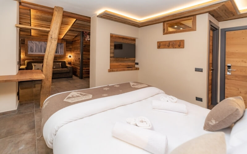 Cozy hotel room with a bed featuring white sheets and a brown snowflake blanket, natural light from a window, inviting atmosphere.