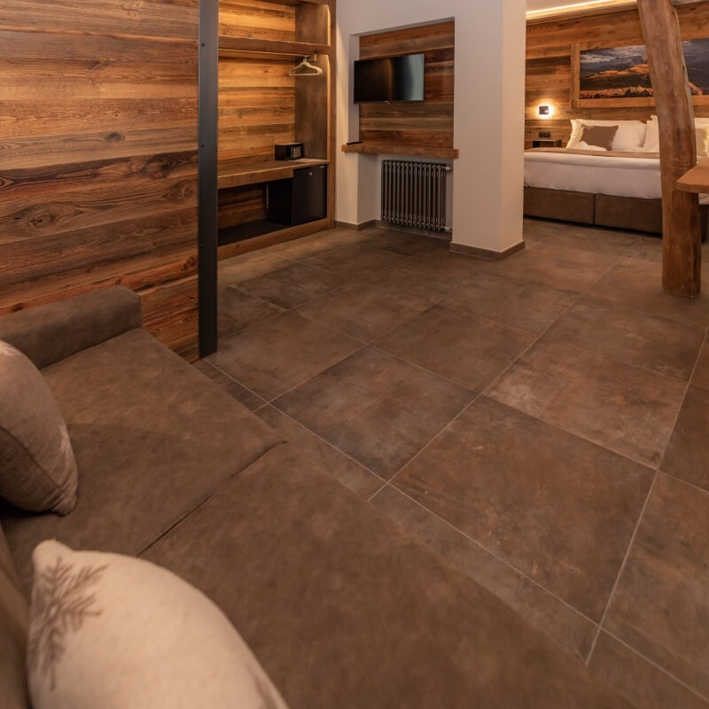 Cozy rustic hotel room with leather couches, a bed, desk, and mountain painting, featuring warm wood and tile accents.