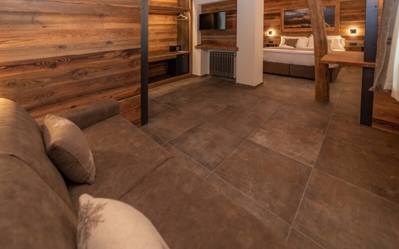 Cozy room with a brown leather couch, white bed, wood paneling, and warm lighting, featuring tile flooring and wall decor.