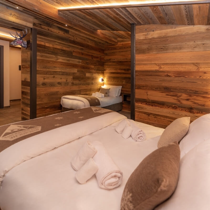 Cozy rustic room with double beds, wood paneling, a deer skull on the wall, and warm ceiling lighting.