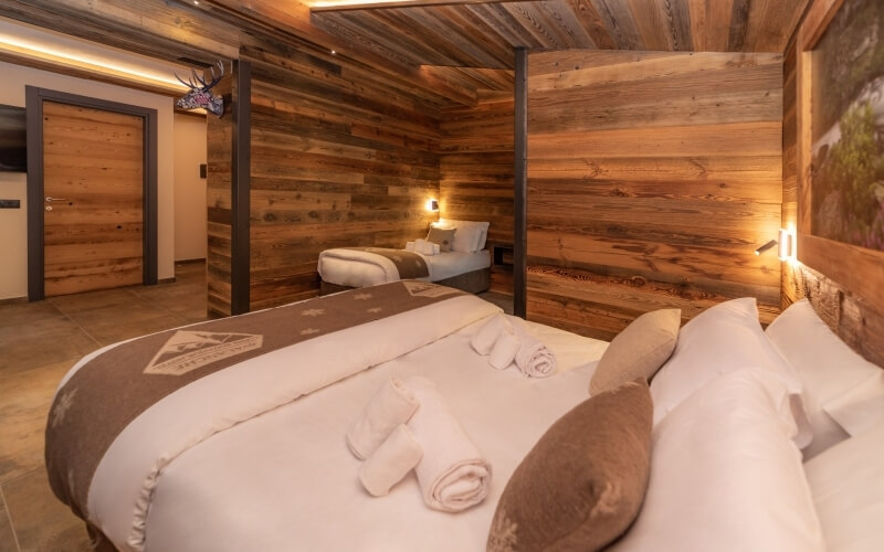 Camera accogliente con due letti, pareti in legno, biancheria bianca e decorazioni calde per un'atmosfera serena.