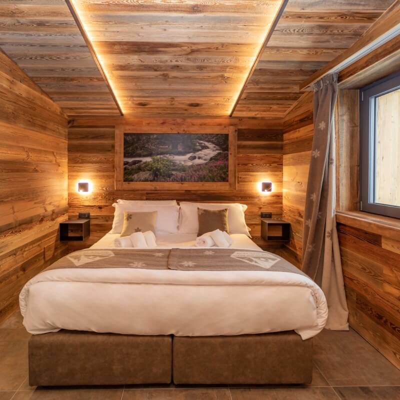 Cozy wood-paneled bedroom with a large bed, river photograph, and warm lighting from nightstands.