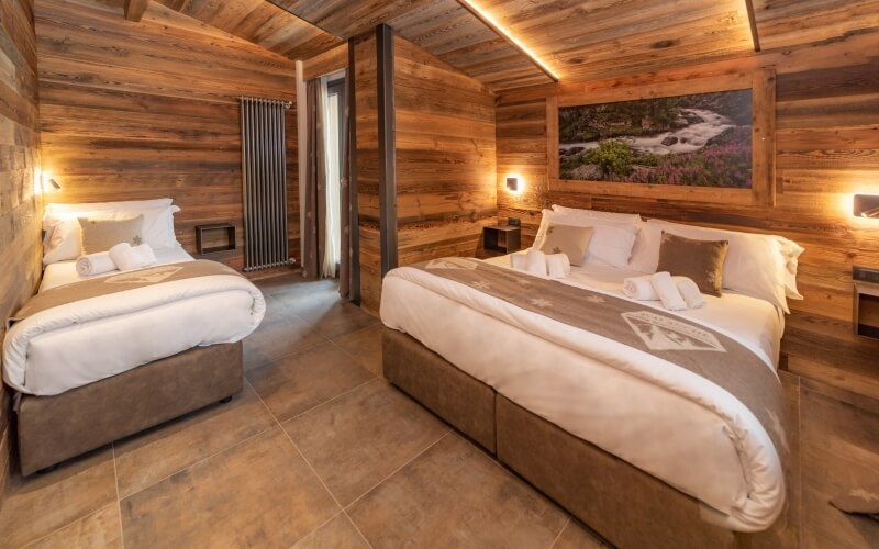 Rustic bedroom with two beds, wooden walls, tiled floor, framed photograph, and decorative elements.