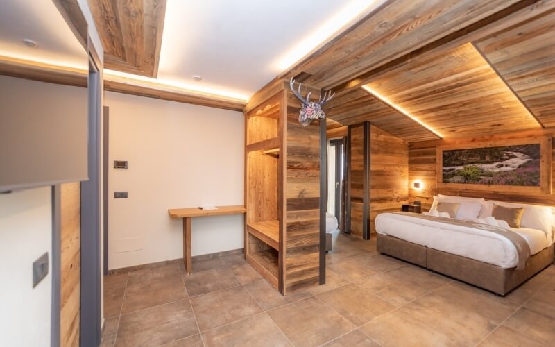 Modern rustic bedroom with a large bed, workspace, wooden accents, and warm lighting, featuring a deer skull and plant decor.