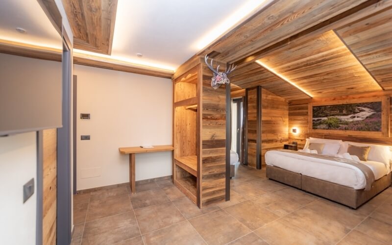 Camera da letto rustica moderna con letto grande, scrivania, lampada calda e pareti bianche, atmosfera accogliente.