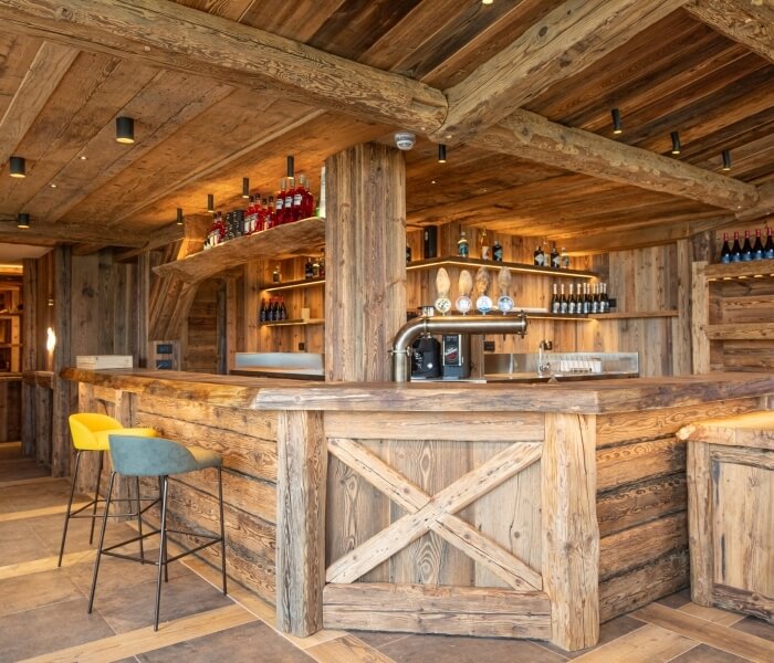 Bar rustico in legno con bancone, scaffali, lavandini e sgabelli colorati, creando un'atmosfera accogliente e informale.