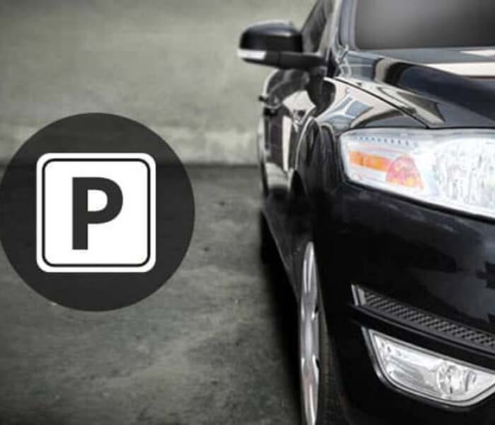 Stylized photo of a dark car's front with a white "P" parking sign on a blurred gray background.
