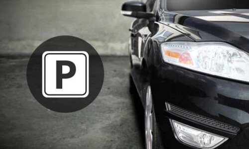 Auto nera lucida parcheggiata su una superficie grigia, con un'icona di parcheggio "P" a sinistra.