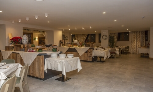 Area pranzo elegante e minimalista con tavoli bianchi, buffet e illuminazione calda, adatta per eventi formali.