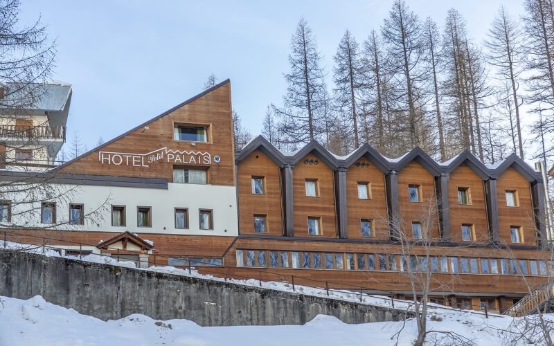 Hotel Palais in snowy mountains, featuring unique architecture with wood paneling, white walls, and peaked roofs.