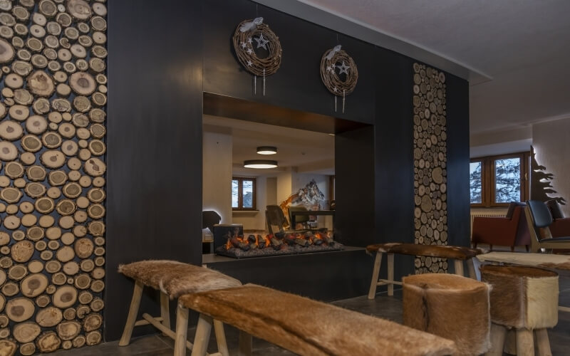 Cozy living room with a black fireplace, circular wreaths, rustic benches, and warm lighting, creating an inviting atmosphere.