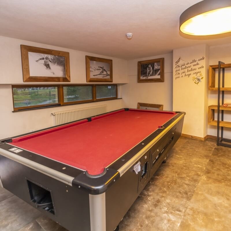 A cozy room featuring a red felt pool table, wooden-framed windows, rustic ski-themed pictures, and a light fixture.