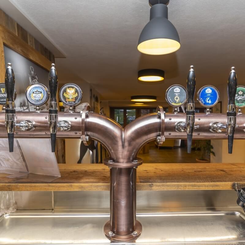 Bar with six beer taps in two rows, wooden counter, black light fixtures, and a doorway to another room in a cozy setting.