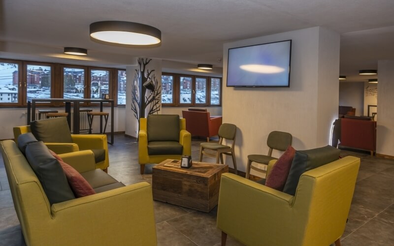 Modern room with yellow and black chairs, a wooden coffee table, a mounted TV, and large windows for natural light.