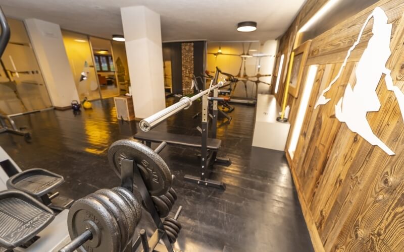 Modern gym with dark wood floor, white walls, exercise equipment, and a silhouette of aerial silks acrobatics on the wall.