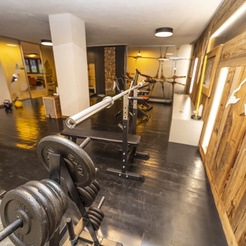 A clean gym with various equipment, a weight rack, a barbell, and an open doorway, featuring a reflective black floor.