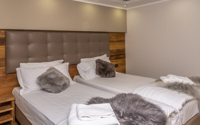 Cozy bedroom with two beds, brown leather headboard, white and gray pillows, and warm lighting.