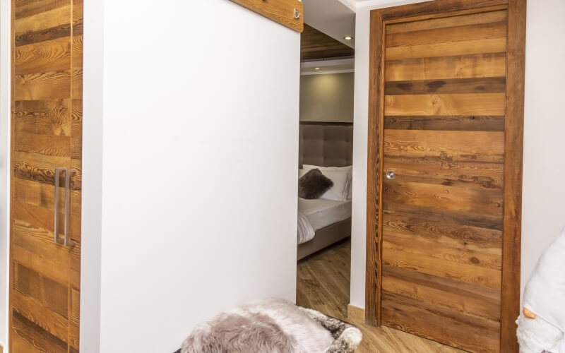Un corridoio bianco con due porte in legno e una camera da letto sullo sfondo, che trasmette un'atmosfera accogliente.