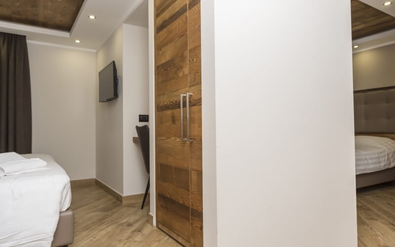 Modern hotel room with two alcove beds, white decor, wooden accents, and a sliding door separating the sleeping areas.