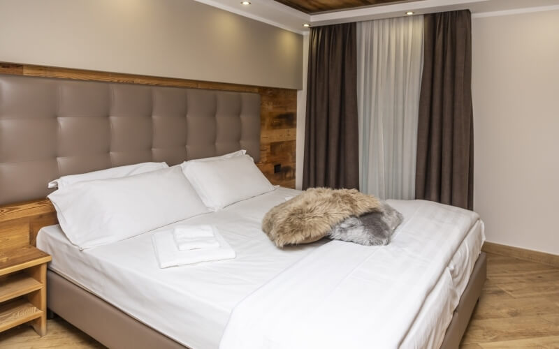 Camera da letto con un grande letto matrimoniale, testiera in pelle marrone, lenzuola bianche e finestra con tende marroni.