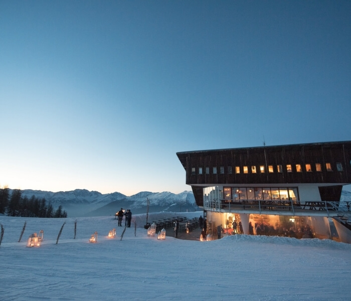 Modern building in a snowy landscape, with warm lanterns, large windows, and misty mountains under a blue sky.