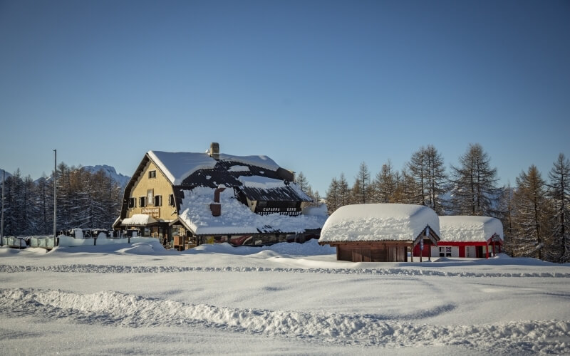 Serene winter scene with a yellow two-story building, a red one-story structure, and mountains under a clear blue sky.