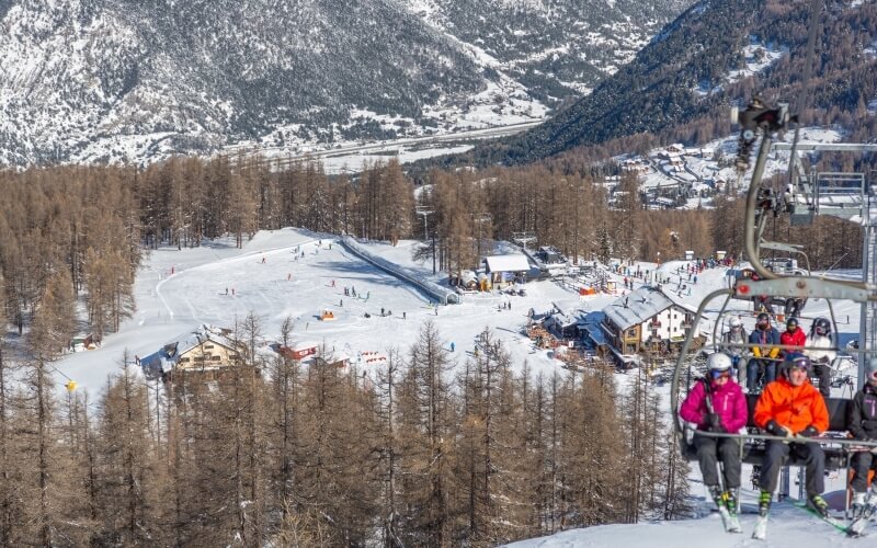 Snowy mountainous landscape with a ski resort, chairlift, and people skiing, creating a lively winter scene.