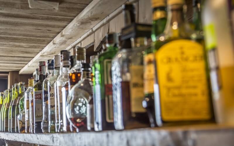 Close-up of a rustic wooden bar shelf with assorted bottles in various sizes and colors, creating a cozy ambiance.