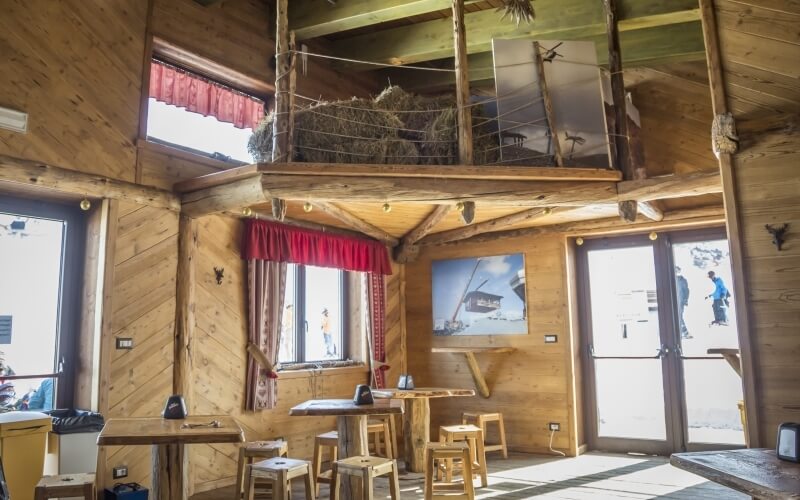 Rustic wooden room with loft, table, chairs, large windows, and beach painting, suggesting a ski lodge atmosphere.