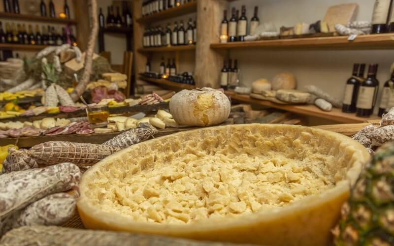 A cozy wine and cheese shop featuring aged cheeses, cured meats, and wine bottles on wooden shelves, warmly lit by candles.