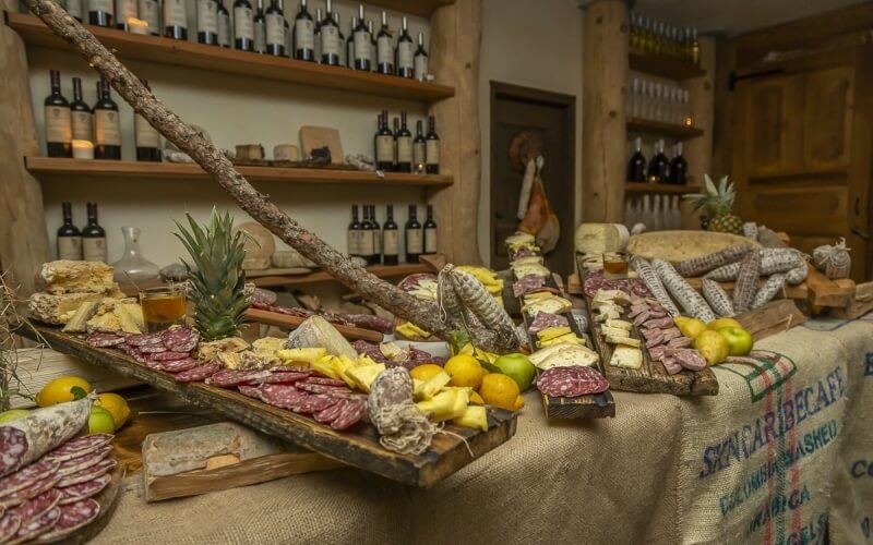 Esposizione elegante di vino, formaggi e salumi su tavolo di legno, con frutta fresca e un ananas, su tovaglia di juta.