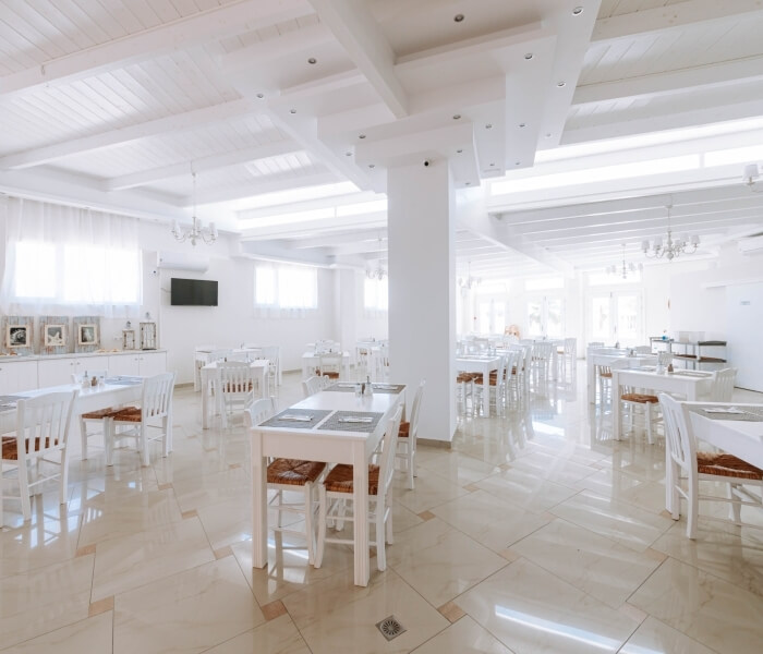 Interno di un ristorante con pareti bianche, tavoli bianchi, luce naturale e decorazioni artistiche.
