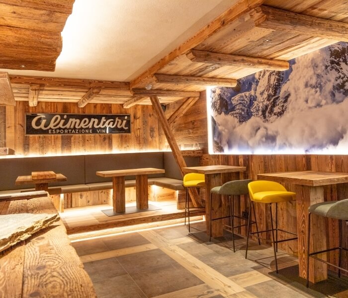 Rustic restaurant interior with wooden accents, mountain mural, and cozy seating, featuring a sign for an Italian wine bar.