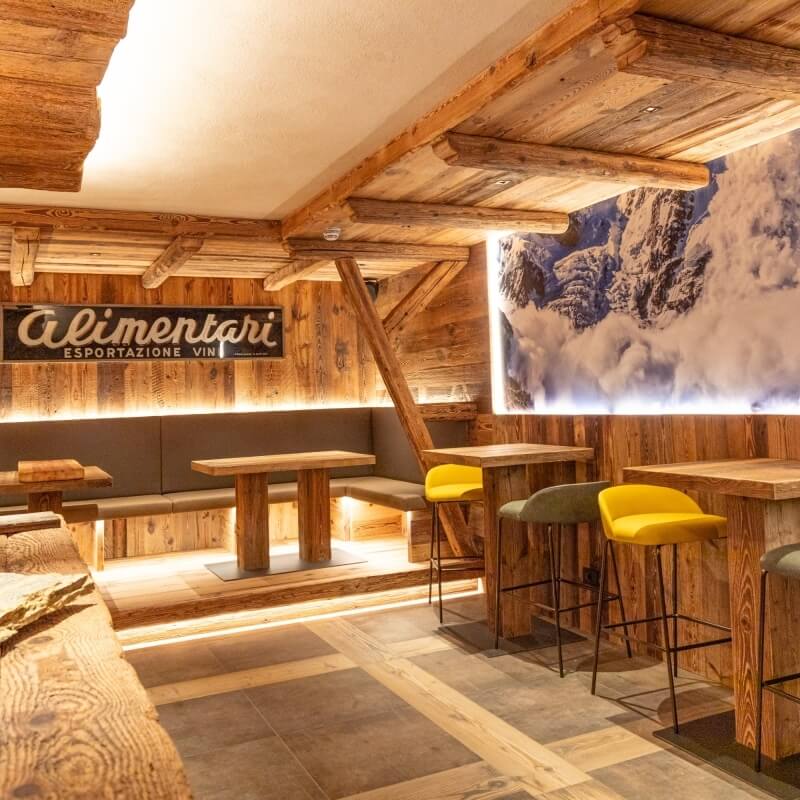 Rustic modern dining area with wooden accents, mountain backdrop, and cozy seating, featuring a sign for "Alimentari ESPORTAZIONE VIN."