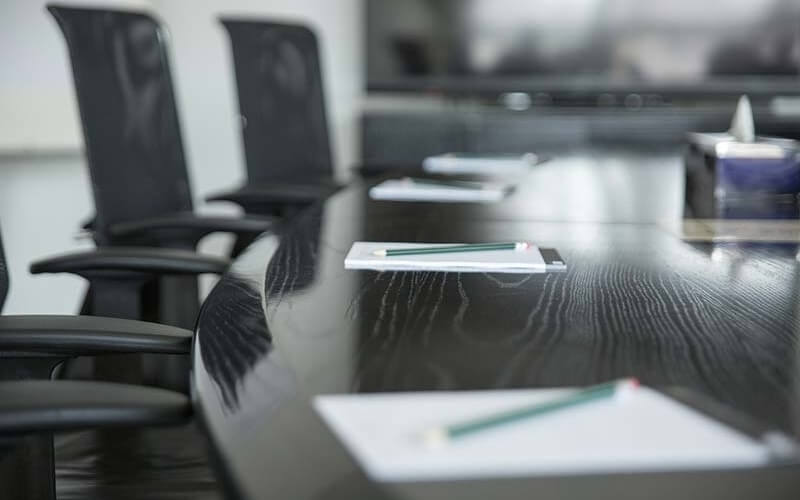 Conference room with a dark wood table, green pencils, papers, and black chairs, suggesting a professional meeting setting.