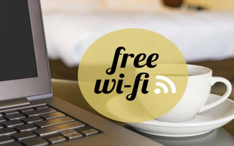 Laptop and coffee cup with a yellow "free wi-fi" circle overlay in a hotel room setting.